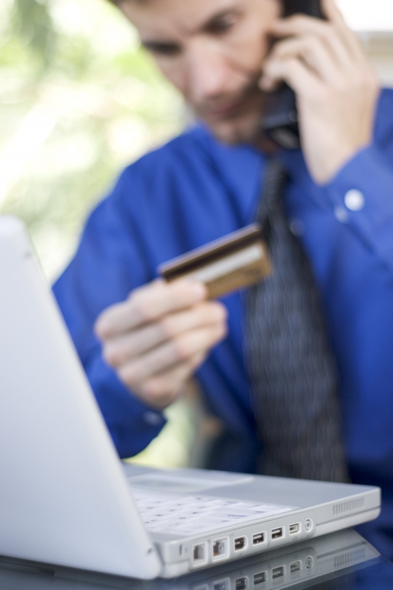 Stock photo of a worried man on the phone, with credit card in hand and laptop in front of him